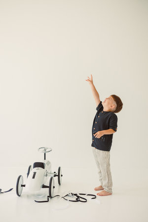 A joyful child reaches for the sky next to a vibrant toy car in a clean studio, enhancing the playful vibeの写真素材