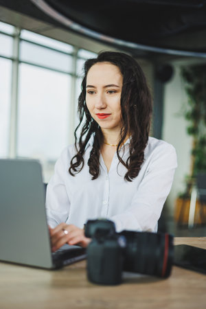 A focused young woman dressed in a crisp white shirt diligently using a laptop in a stylish and modern office settingの写真素材