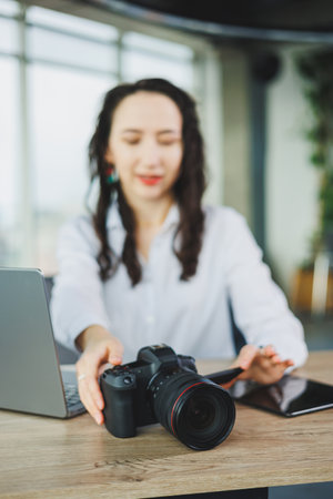 A dedicated and focused professional woman actively engages with her camera while working in a stylish office settingの写真素材