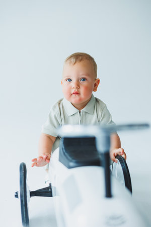 A playful baby sits beside a stylish toy car, capturing innocence and joy in a minimalistic backdrop.の写真素材