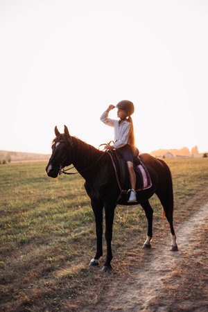 A young girl is having a wonderful time horseback riding during a beautiful sunset in a serene landscapeの写真素材