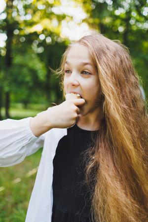 A young girl with long hair is playfully enjoying a snack while outdoors, blissfully surrounded by natureの写真素材