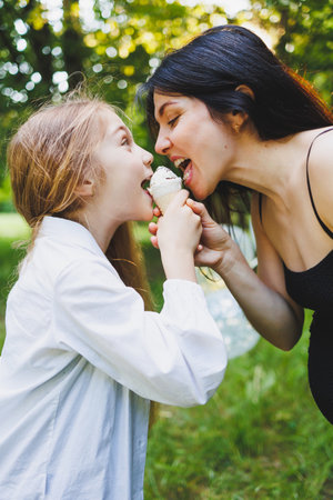 A joyful moment of a child and a loving woman sharing ice cream outdoors, capturing playful affection and happinessの写真素材