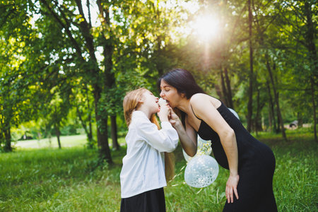A loving mother cherishes a beautiful, precious moment with her daughter in a lively, joyful, sunlit green parkの写真素材