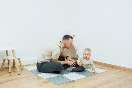 A loving father energetically plays and interacts with his adorable baby on a soft mat in a cozy, warm roomの写真素材