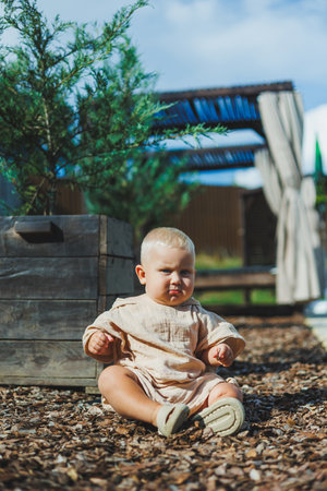 A lovely baby joyfully sits on the gravel outdoors, surrounded by abundant greenery, showcasing pure innocence and joyの写真素材