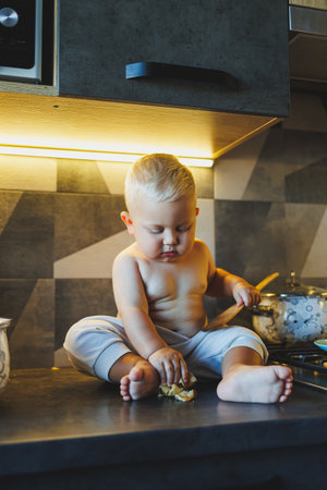 A curious little toddler joyfully sits atop a kitchen counter, eagerly exploring various foods with a playful demeanorの写真素材
