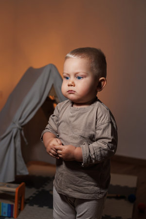 A cute little toddler stands thoughtfully in a cozy indoor space, filled with warmth, innocence, and joyの写真素材