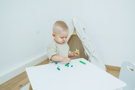 A little one-year-old boy is sculpting plasticine while standing at the table. The child is playing with educational toys.の写真素材