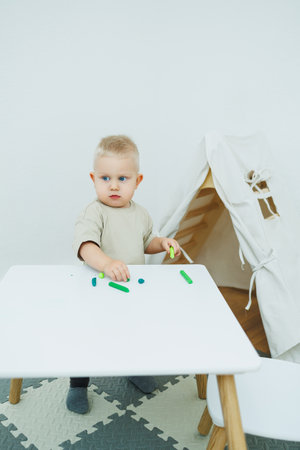 A little one-year-old boy is playing with modeling clay while standing at the table.の写真素材