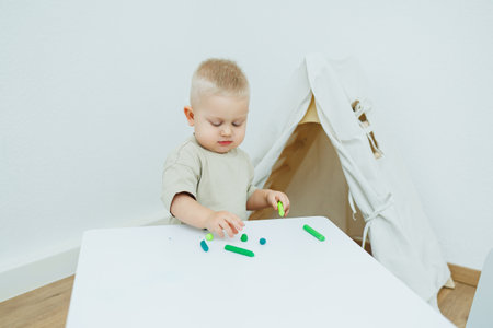 A little one-year-old boy is sculpting plasticine while standing at the table. The child is playing with educational toys.の写真素材