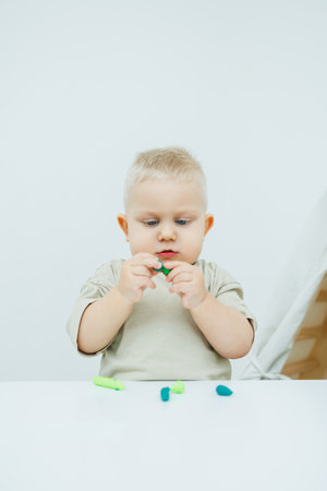A little one-year-old boy is sculpting plasticine while standing at the table. The child is playing with educational toys.の写真素材