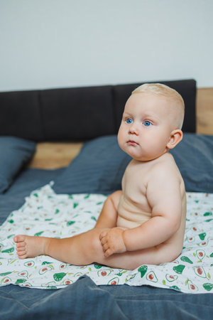 An adorable baby is seated comfortably on soft bedding, showcasing pure joyful innocence and vivid curiosityの写真素材