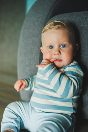 A charming baby with bright blue eyes in a striped outfit, looking playful and relaxed in a cozy indoor spaceの写真素材