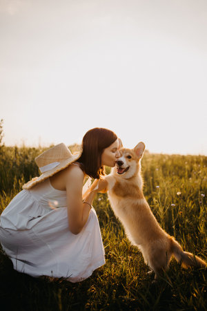 Cute young woman in a white dress playing with her dog at sunset. Summer walk with a dog. Man's best friend is a cute dog.の写真素材