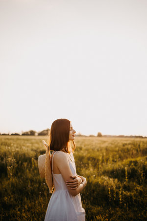 Woman in a field at sunset. Happy carefree woman in a dress in a large field, at sunset. Walking under the setting sun in natureの写真素材