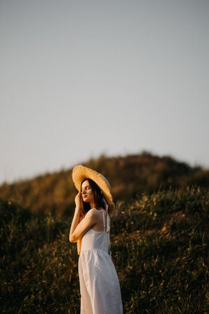 Woman in a field at sunset. Happy carefree woman in a dress in a large field, at sunset. Walking under the setting sun in natureの写真素材