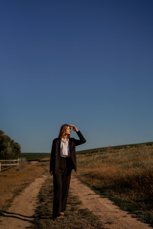 Woman in a field at sunset. Happy carefree woman in a black dress in a large field, at sunset. Walking under the setting sun in natureの写真素材