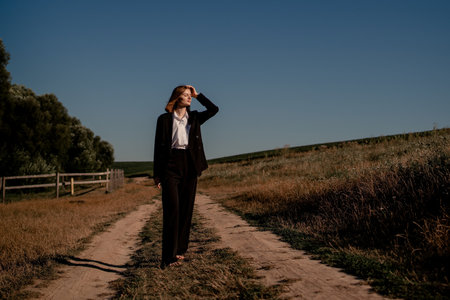 Woman in a field at sunset. Happy carefree woman in a black dress in a large field, at sunset. Walking under the setting sun in natureの写真素材