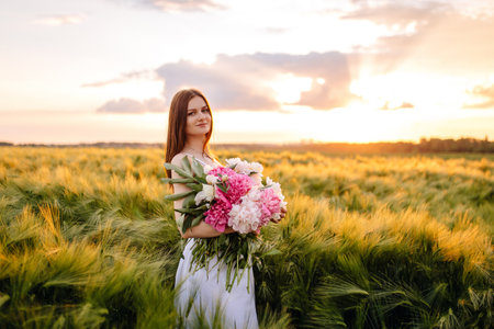 A tranquil bride elegantly holding a vibrant bouquet amidst vast golden fields under a beautiful sunset skyの写真素材