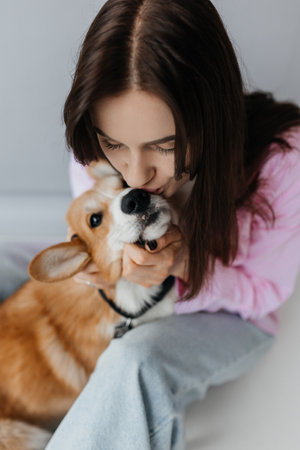 In a cozy indoor environment, a woman gently kisses her playful corgi, clearly showcasing their deep bondの写真素材