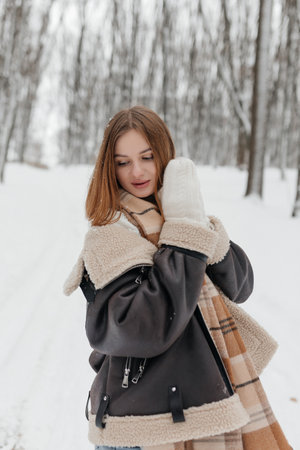 A woman, dressed in a cozy winter outfit, joyfully embraces the enchanting beauty of the snowy woods around herの写真素材
