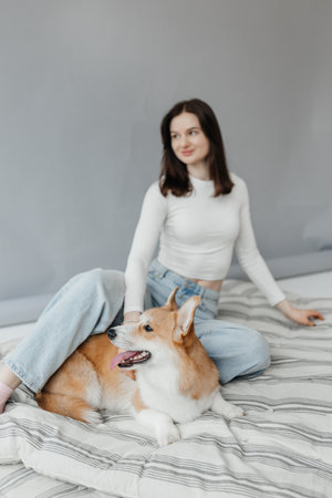 A relaxed young woman poses happily with her cheerful corgi on a beautifully patterned bed, enjoying the momentの写真素材