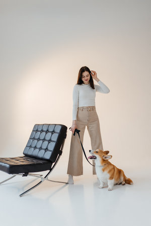 In a sleek and minimalist space that is ideal for modern living, a stylish woman poses with her adorable corgiの写真素材