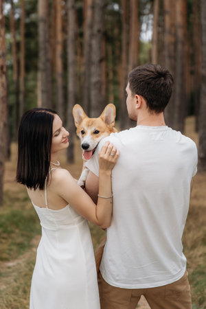 A blissful couple holds their adorable corgi in a tranquil forest, showcasing their love and companionshipの写真素材