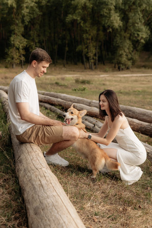 A cheerful couple is joyfully playing with their adorable dog in a serene outdoor setting, surrounded by lush natureの写真素材