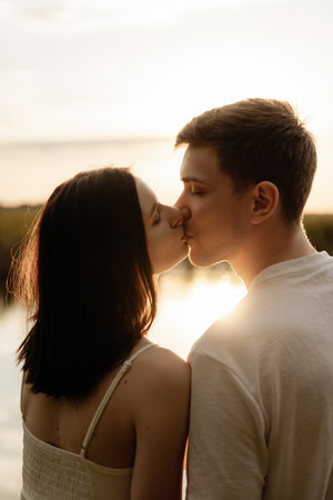 A romantic couple is sharing a tender kiss against a stunningly beautiful sunset by the waters edgeの写真素材