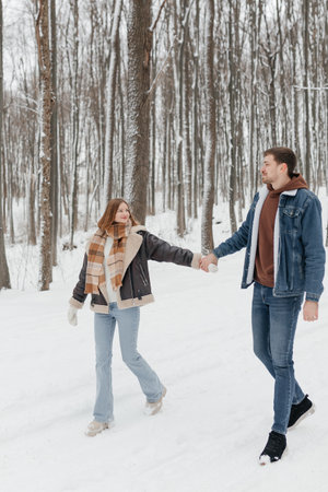 A joyful couple strolls hand in hand through a snowy forest, beautifully capturing love during wintertimeの写真素材