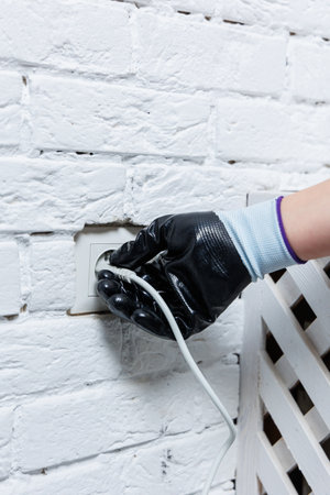 A person who is wearing a protective glove is carefully connecting a cable to an outlet situated on...