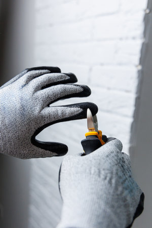 A person who is wearing protective gloves is holding a sturdy pair of pliers firmly in their hand, prepared for work or fixing somethingの写真素材