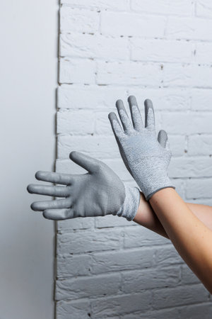 A person dressed in a stylish pair of grey gloves stands in front of a clean, white brick wall, creating a striking visual contrastの写真素材