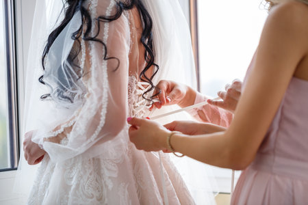A woman is assisting a bride with her preparations for the beautiful and special occasion of her wedding ceremonyの写真素材