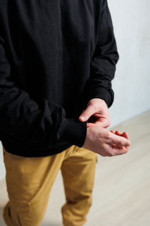A closeup of a person adjusting their black sweater and tan pants in an elegant and stylish settingの写真素材