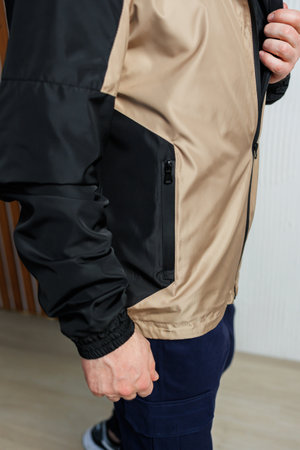 A man can be seen wearing a stylish black and tan jacket that features a convenient zipper, making...