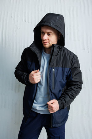 A man is dressed in a stylish black jacket that features a hood, perfect for various weather conditions, providing both warmth and styleの写真素材