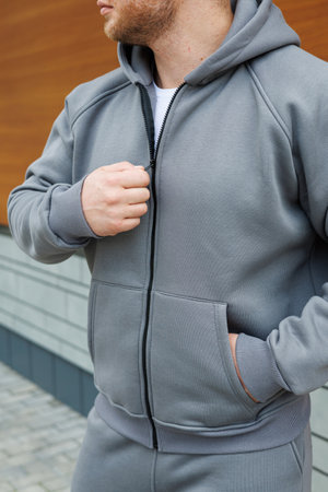 A man, dressed in a stylish grey hoodie, stands casually with his hands placed comfortably in the pockets of his hoodie garmentの写真素材