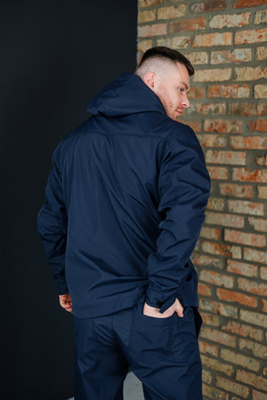 A man dressed in a blue jacket is standing confidently in front of an old brick wall that shows signs of wear and ageの写真素材