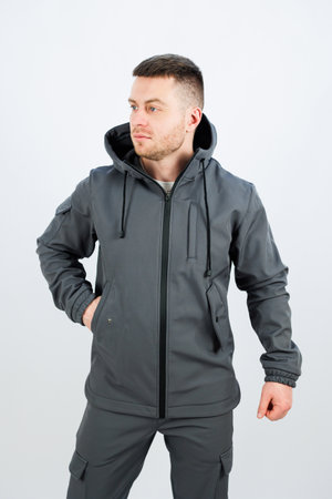 A man with a neatly trimmed beard is wearing a stylish grey jacket that features a functional hood for additional warmth and protectionの写真素材