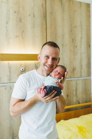In a warmly lit and inviting bedroom, a proud father gently cradles his precious newborn, embodying the pure joy of parenthood and the deep love that binds their family togetherの写真素材