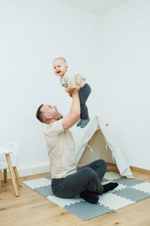 A joyful father lifts his happy baby in a cozy indoor play area, capturing a delightful moment of bonding, filled with laughter, love, and cherished memories shared togetherの写真素材