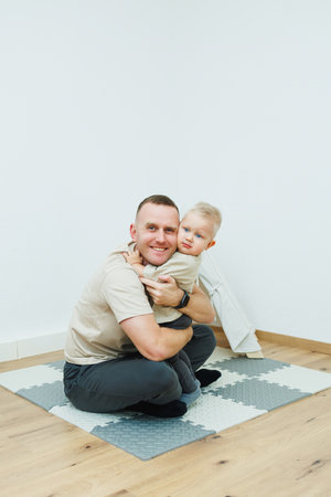 A heartwarming moment has been beautifully captured of a father joyfully embracing his young child in a bright, minimalist room, emphasizing the warmth and love of family bondsの写真素材