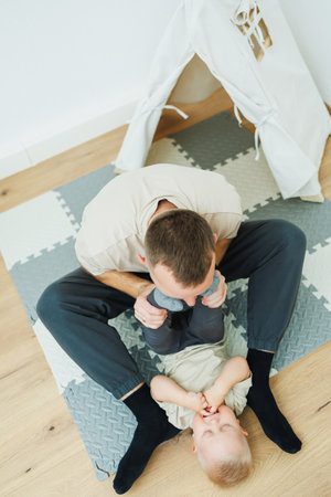 A joyful father playfully engages with his young child on a soft mat, highlighting their bond in a warm, cozy indoor environment filled with laughter and happinessの写真素材