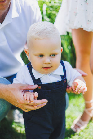 A cute toddler in fashionable overalls joyfully walks handinhand with a family member in a bright, sunny outdoor setting, capturing heartwarming family momentsの写真素材