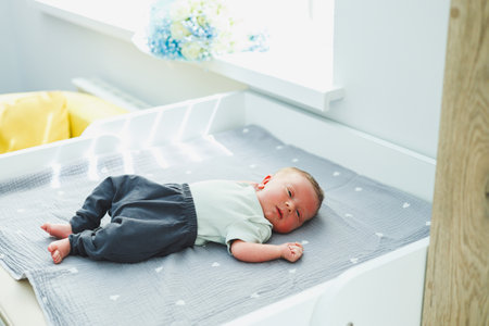 In a bright and cheerful nursery, a lovely newborn baby lies peacefully on a cozy gray blanket, capturing a joyful and heartwarming moment for the entire family to cherishの写真素材