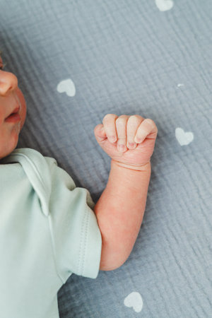 A closeup of a newborns tiny hand in a soft pastel onesie, resting on a heartpatterned blanket, symbolizes pure innocence and love in the early moments of lifeの写真素材