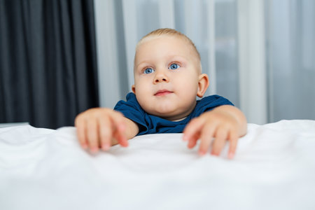 An adorable little baby with striking blue eyes and short hair is reaching out while curiously exploring a cozy room environment, beautifully showcasing innocence and pure wonderの写真素材